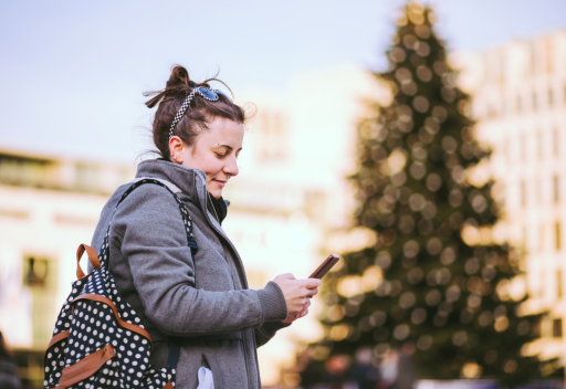 A woman is checking her email on her phone as a Christmas tree stands in the background.
